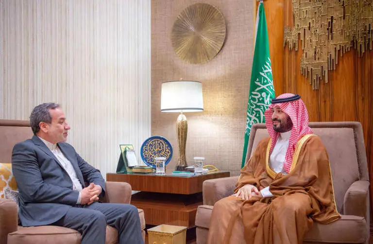 Saudi Crown Prince MBS and Iranian Foreign Minister Araqchi shake hands in an ornate room, both wearing traditional robes during a diplomatic meeting in Riyadh.