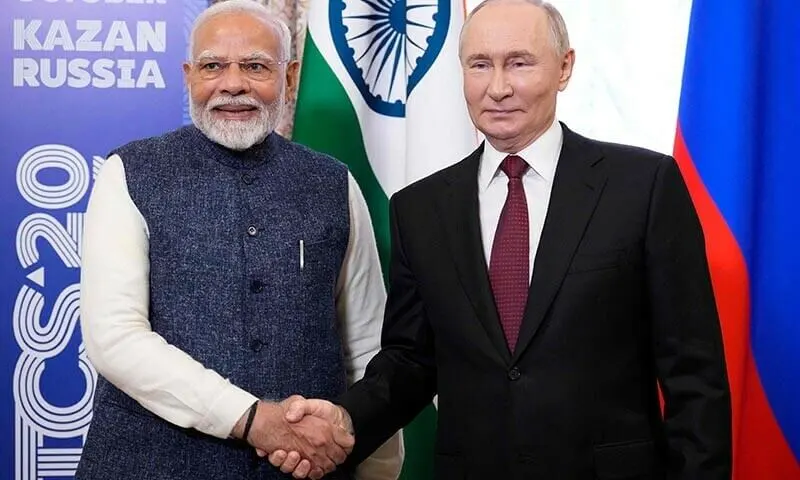 Russian President Vladimir Putin and Indian Prime Minister Narendra Modi seated in formal attire at a meeting table, engaged in conversation.