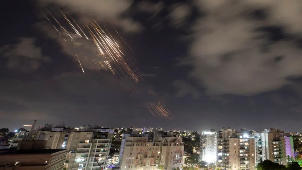 Night sky filled with missile trails and explosions as Iran launches ballistic missiles towards Tel Aviv, Israel's defense systems activate.