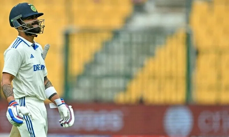 A dejected Virat Kohli walks off the field with his head down, carrying his bat under his arm, as he returns to the pavilion through the boundary rope.