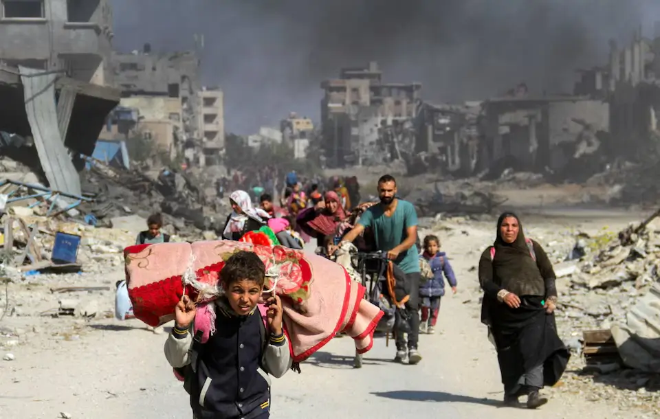 Groups of Palestinian civilians walk with belongings through devastated streets of Gaza City while fleeing northern Gaza amid Israeli military operations.