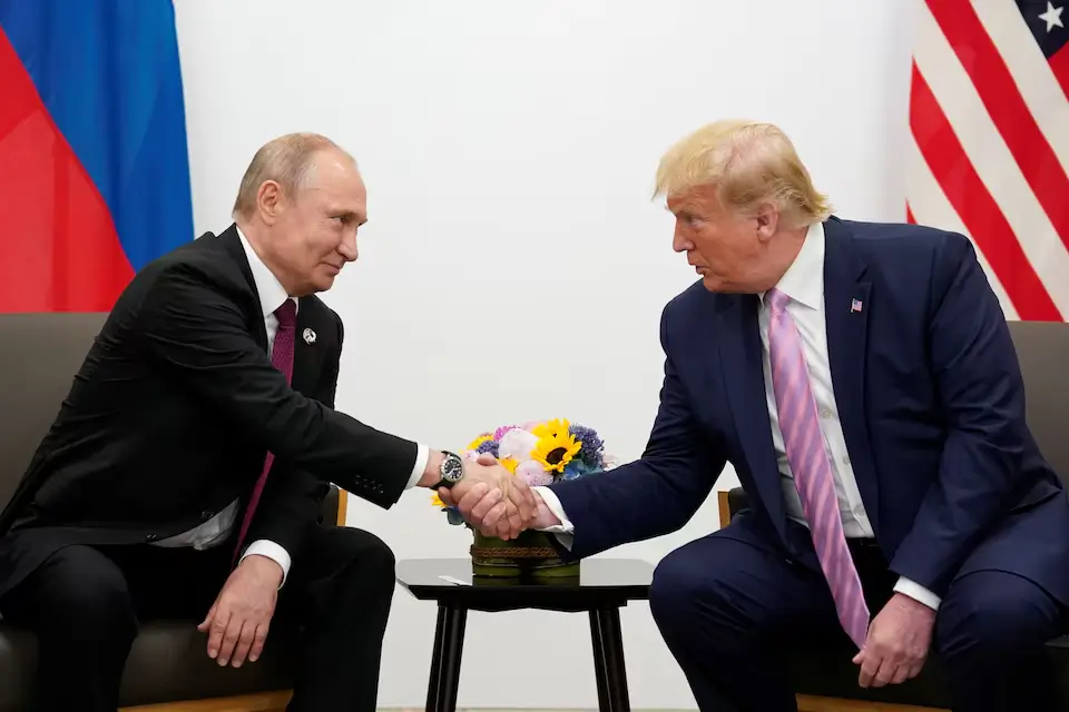 Putin and Trump engage in a firm handshake, both in dark suits, while seated in ornate chairs during their bilateral meeting at the G20 summit.