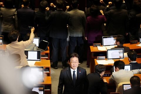 Lee Jae-myung walks past People Power Party lawmakers protesting during impeachment vote of Han Duck-soo at the National Assembly.