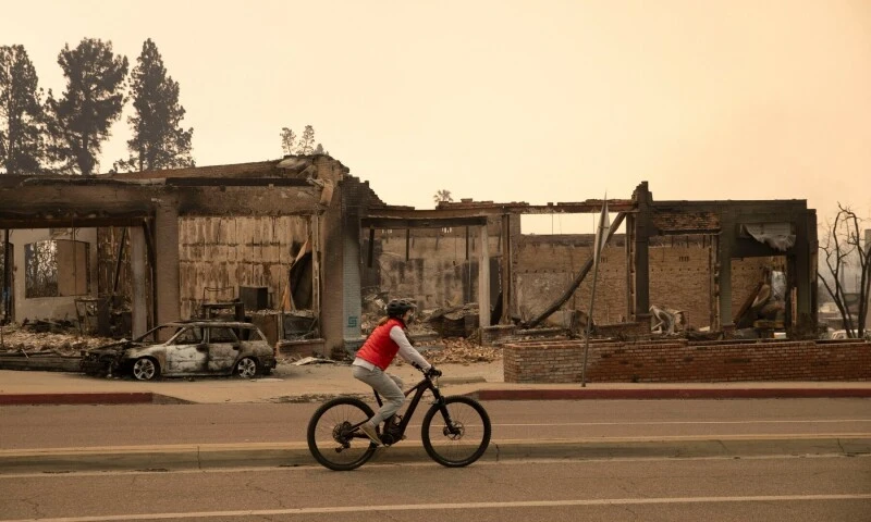 A bicyclist rides past damaged buildings affected by wildfires in Altadena, California, January 9, 2025, during Los Angeles wildfires.