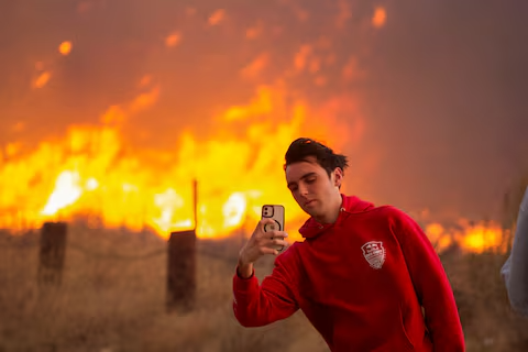 With heavy smoke in the air, a man uses his cell phone while the Hughes Fire burns close to Castaic Lake in Southern California.